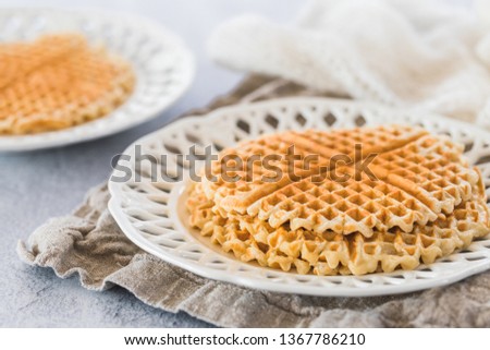 Fresh swedish golden waffles with nothing on top. White patterned plate, gray background and a piece of linen cloth underneath the plate. There is another plate defocused in the background.