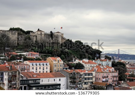 Sao Jorge Castle on a hill overlooking  a cluster of buildings of Lisbon city, Portugal with Tejo river and bridge in the background