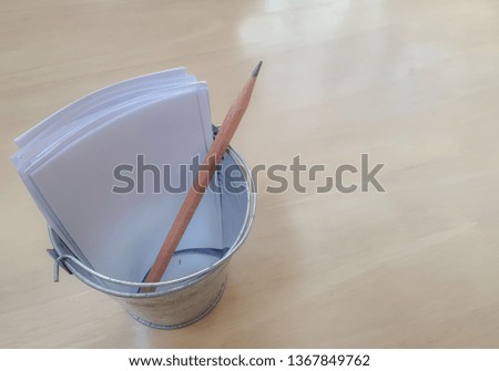 Pencil and white papers in the tiny steel pencil holder places on the light wooden table. The plain white papers for taking note.