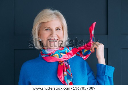 Aged lady style. Accessories. Wardrobe essentials and fashion trends. Smiling female in blue pullover touching neckerchief. Royalty-Free Stock Photo #1367857889