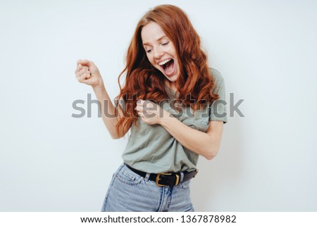 Happy young woman partying and dancing as she laughs and enjoys herself in front of a white wall with copy space