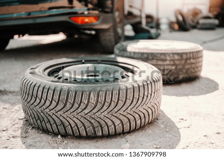 Picture of old tire on ground at auto mechanic workshop. In background car.