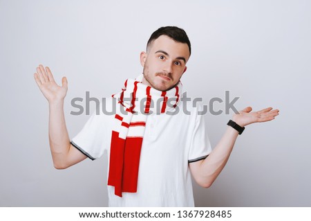 Photo if young man doing unknown gesture, wearing a sarf and standing over white wall 