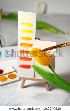 Conceptual image of watercolour palette, brushes and yellow tulip on easel. Spring concept