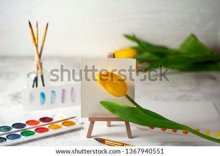 Conceptual image of watercolour palette, brushes and yellow tulip on easel. Spring concept