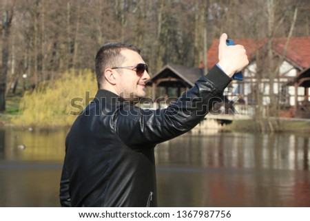 man in sunglasses and a black jacket makes a selfie by the lake