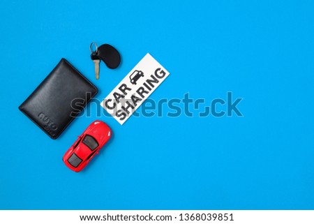 Car sharing concept. Composition with driver's license, vehicle key, toy car, text sign "CAR SHARING" on blue background. Top view. Taxi alternative, temporary car rental, sharing economy