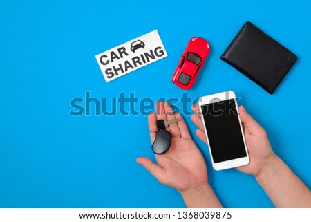Car sharing app concept. Toy car, auto drive license, human hand with smartphone and car key, text sign "CAR SHARING" on blue background. Flat lay composition. Top view.