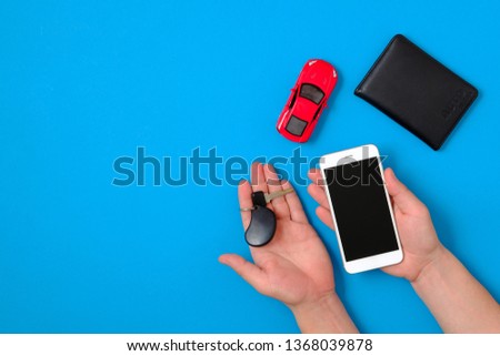 Car rental app concept. Toy car, auto drive license, human hands holding smartphone and car car key on blue background. Flat lay composition. Top view.