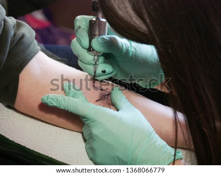 tattoo master makes a tattoo. close-up of hands and typewriter. green gloves. close up.