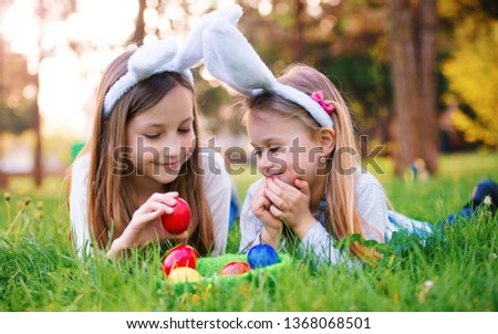 Easter. Two little girls with a bunny ears and colorful eggs have fun in the meadow