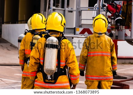 Firefighter team and extinguish tank working on the fire site.Fireman protection suit uniform for ready working.Rescue doing teamwork against fire.A group of firemen attacking a fire with water.