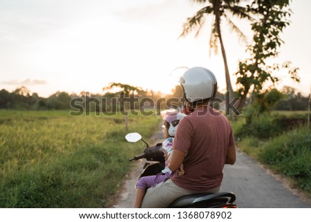 asian father and child look at sunset while riding motorbike scooter