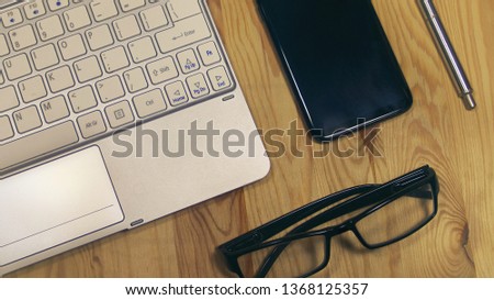 Flat lay a wooden office desk with a keyboard, smartphone, glasses and a pen.