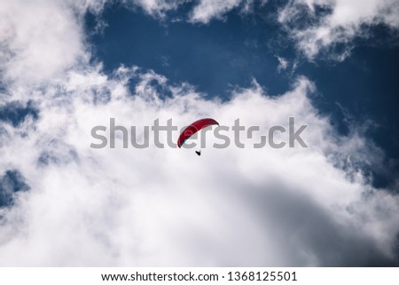 One man in a paraglider flies in a cloudy blue sky