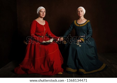 Two sisters (twins) in medieval costumes play the nobility. Evening reading of the prayer (bible). Medieval entertainment, hobby