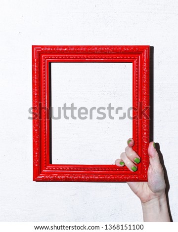 Female hand holds red frame.  Vintage photo frame. Red frame on white background. Concrete wall. Space for text.