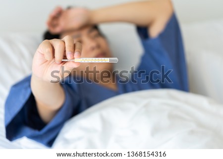 Asian handsome man Hypothermia has been measured by fever. Lie on the bed to give a body of rehabilitation. The concept of medical care to patients at home by yourself. Royalty-Free Stock Photo #1368154316