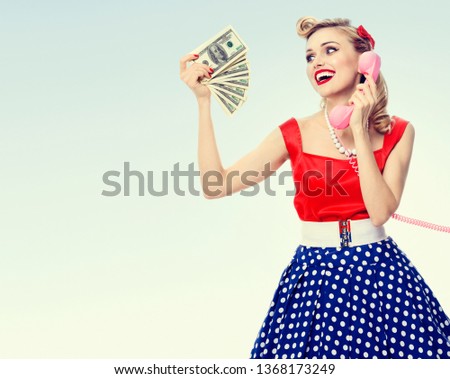 Bright photo of happy woman with money, talking on phone, dressed in pin-up style dress in polka dot, with blank copyspace area for text or slogan. Caucasian blond model in retro fashion concept.