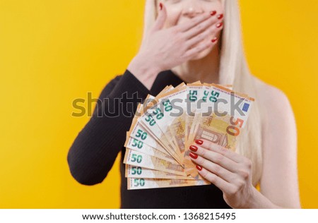 Money, cash in hand. Young blonde girl holding money banknotes isolated over yellow background.