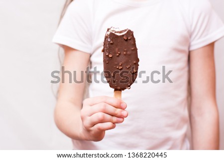 The girl holds in her hand a bitten popsicle in chocolate icing with nuts
