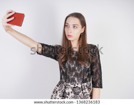 cute caucasian friendly girl stands with a mobile phone in her hand and takes a happy emotional selfie on a white background in the Studio alone