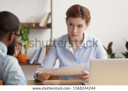 Angry female boss dissatisfied with bad financial result in report demand explanation from stressed incompetent african employee scolding upset intern for mistake in paperwork having conflict at work Royalty-Free Stock Photo #1368244244