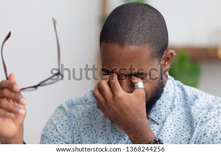 Tired african businessman taking off glasses rubbing dry irritated eyes feeling fatigue headache pain eyestrain, black overworked man massage nose bridge suffer from bad weak vision problem tension Royalty-Free Stock Photo #1368244256