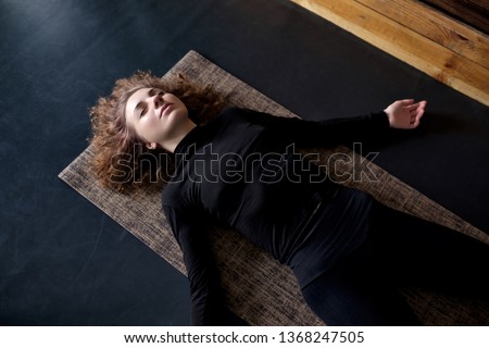 woman practicing in a yoga studio resting in shavasana or corps pose Royalty-Free Stock Photo #1368247505