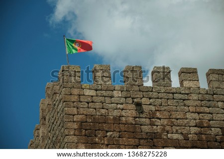 Portuguese flag fluttering on top of stone tower, in a sunny day at the Linhares da Beira Castle. A medieval hamlet with unique architectural diversity fruit of several times, in eastern Portugal.