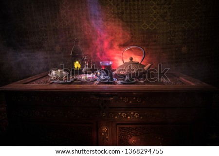 Arabian tea in glass with eastern snacks on vintage wooden surface. Eastern tea concept. Low light lounge interior with carpet. Empty space. Selective focus.