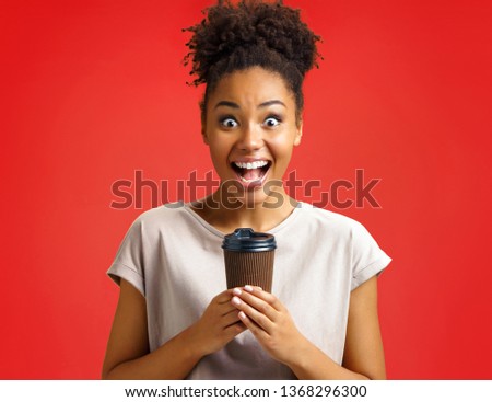Joyful girl holds cup of hot coffee. Photo of african american girl wears casual outfit on red background. Emotions and pleasant feelings concept.