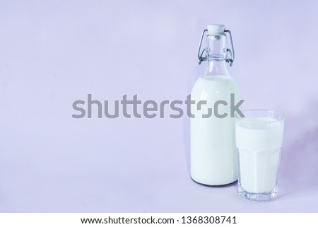 Fresh milk for breakfast in a glass bottle and a glass of milk on a lavender background. space for text