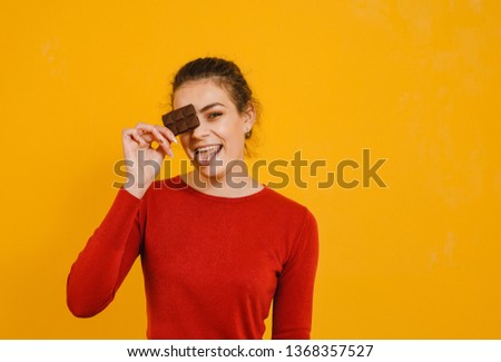 A brunette girl who eats chocolate and shows gestures and is happy over a yellow background