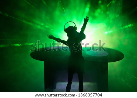 Dj club concept. Woman DJ mixing, and Scratching in a Night Club. Girl silhouette on dj's deck, strobe lights and fog on background. Creative artwork decoration with toy. Selective focus