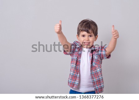 Picture of cute boy child standing isolated over grey background gesturing with hands and show thumbs up. Looking camera.