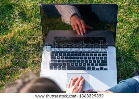 Young woman lying and relax on green grass in park summer day while using laptop.