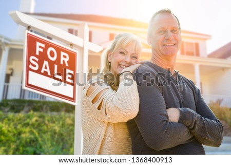 Attractive Middle-aged Couple In Front House and For Sale Real Estate Sign.