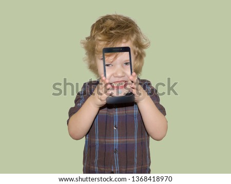 A boy kid looks into the camera of a smartphone, shows the screen with his digital photo. Toddler smiles at the camera and takes a selfie.