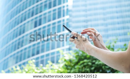 Women's hands use a smartphone on the background of a glass business center and green trees