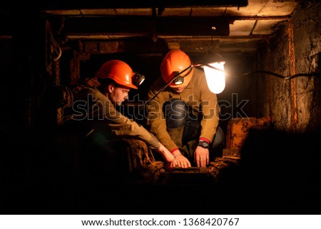 Two young guys in a working uniform and protective helmets, sitting in a low tunnel. Workers of the mine. Miners Royalty-Free Stock Photo #1368420767