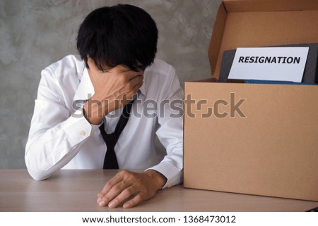 The image of a businessman sitting tense, disappointed, tired, pressured by executives. There is a resignation letter placed in the box for personal storage. 