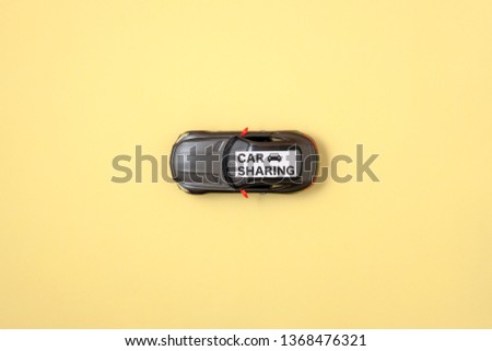 Car sharing concept. Modern toy car model and text sign "CAR SHARING" on yellow background. Carsharing, auto dealership and rental, sharing economy, taxi alternative, ride sharing. Top view. Flat lay.