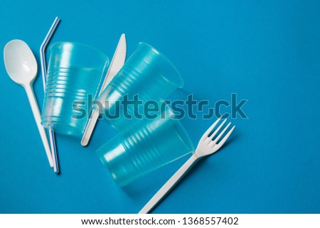 White single-use plastic knife, spoon, fork and plastic drink straws on a blue background. Say no to single use plastic. Environmental, pollution concept. Royalty-Free Stock Photo #1368557402