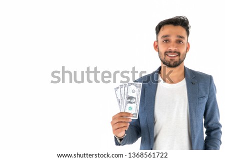 Successful Indian entrepreneur with dollar banknotes in hand classical suit look at camera with toothy smile while standing against. Young businessman hold lot bunch of dollars banknotes, cash money.