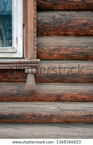 A fragment of a window on a wooden wall of an old house. Wood carvings adorn the platband of an old window. The walls of the house of painted boards close-up. Old building.