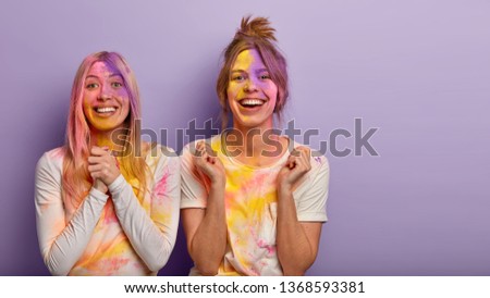 Religious spring holiday in India. Cheerful overjoyed two women have time for play of colors, look crazy, apply special colourful powder on face and clothes, happy after having excting merry day Royalty-Free Stock Photo #1368593381