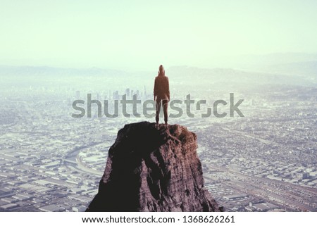Back view of young person on mountain top on blurry city background. Leadership and career concept