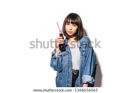 Picture of young woman in jeans jacket drinking soda standing isolated over grey wall background.