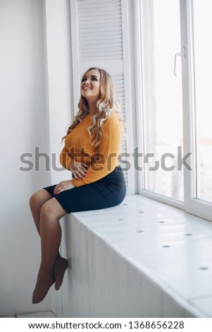Elegant woman in a yellow sweater. Pregnant woman sitting near window
